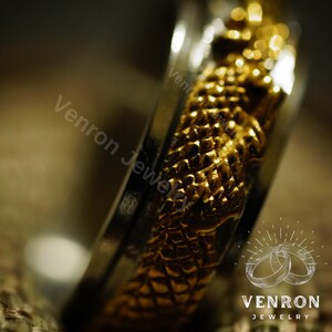 May include: A gold and silver ring with a textured design. The ring is a close-up and the design is in focus. The ring is a wedding band.