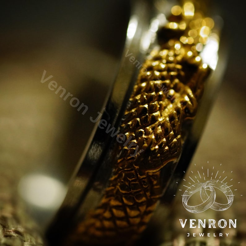 May include: A gold and silver ring with a textured design. The ring is a close-up and the design is in focus. The ring is a wedding band.