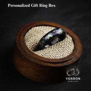 May include: A black ring with iridescent opal inlay in a wooden ring box. The box has a brown fabric lining and the Venron Jewelry logo is visible on the bottom.