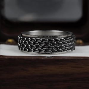 May include: A silver ring with a textured, scaly design. The ring is in a wooden box.