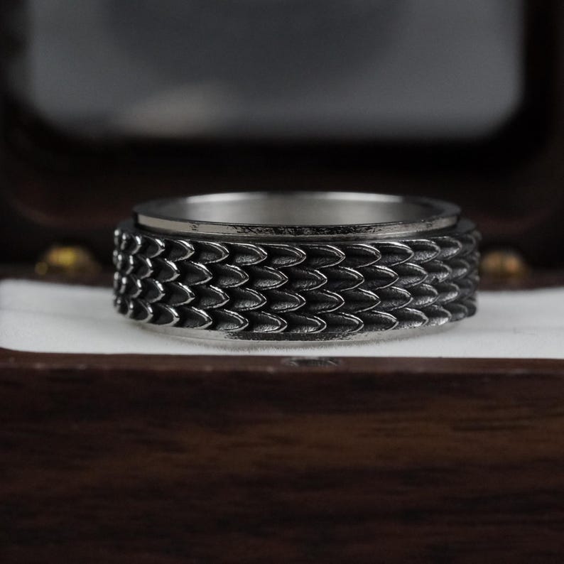 May include: A silver ring with a textured, scaly design. The ring is in a wooden box.