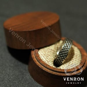 May include: A silver ring with a braided design sits in a wooden ring box with a beige fabric lining. The box is engraved with the text "Venron Jewelry".