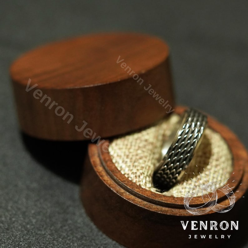 May include: A silver ring with a braided design sits in a wooden ring box with a beige fabric lining. The box is engraved with the text "Venron Jewelry".