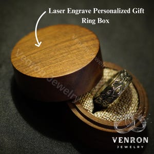 May include: A wooden ring box with a lid that can be engraved with a personalized message. The box is open and a gold ring with a detailed design is inside. The box is made by Venron Jewelry.