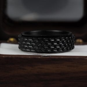 May include: A black ring with a textured, scaly design. The ring is in a wooden box.