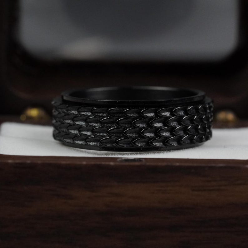 May include: A black ring with a textured, scaly design. The ring is in a wooden box.