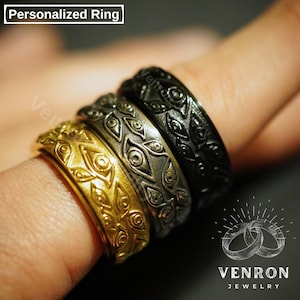 May include: Three gold and black rings with an eye design. The rings are stacked on a finger. The rings are engraved with the word "VENRON JEWELRY".