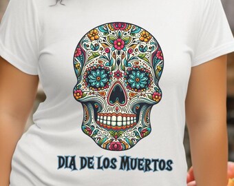 May include: White t-shirt featuring a colorful sugar skull design with floral and decorative elements. The text "DIA DE LOS MUERTOS" is printed below the skull. The shirt is a crew neck style.