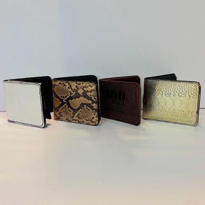 May include: Four bi-fold wallets in a row, each with a different design. The wallets include a white one with black stitching, a snakeskin pattern, a dark brown ostrich skin, and a gold-toned embossed leather.