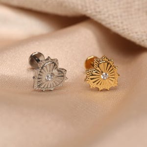 May include: Two heart-shaped earrings with a small diamond in the centre. The earring on the left is silver and the earring on the right is gold.