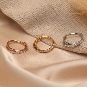 May include: Three hoop earrings with a single row of clear cubic zirconia stones. The hoops are in gold, rose gold, and silver.