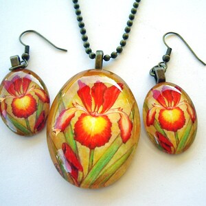 May include: A jewelry set featuring a pendant necklace and matching earrings. The oval-shaped pieces display a vibrant watercolor iris design in red, yellow, and green. The set has a bronze-colored chain and earring hooks.