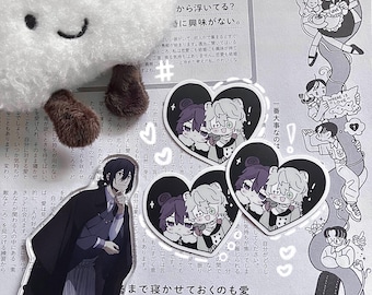 May include: A black and white illustration of two characters in a heart-shaped frame. The characters are wearing black and white clothing and have purple hair. The illustration is printed on a sticker.