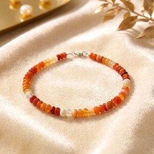 Può includere: Un braccialetto di perline con piccole perle rotonde nei toni dell'arancione, del rosso e del bianco. Le perle sono infilate su una catena d'argento con una chiusura. Un accessorio colorato e delicato.