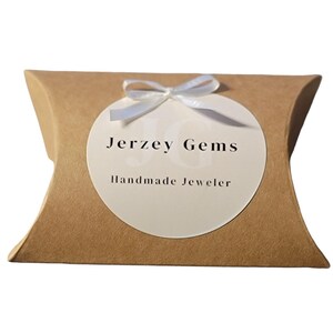 Jerzey Gems Branded Packaging Pillow Box for Rings with small white bow over Jerzey Gems Handmade Jeweler