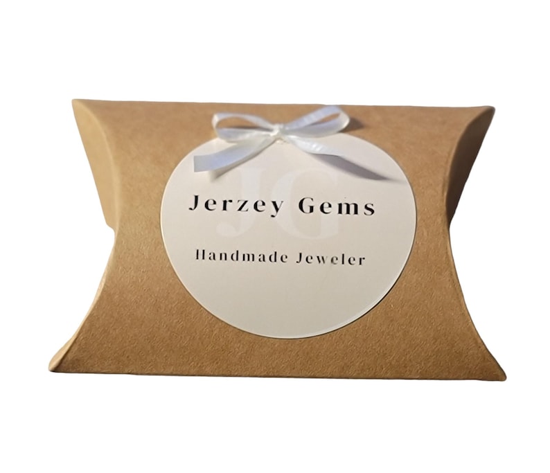 Jerzey Gems Branded Packaging Pillow Box for Rings with small white bow over Jerzey Gems Handmade Jeweler