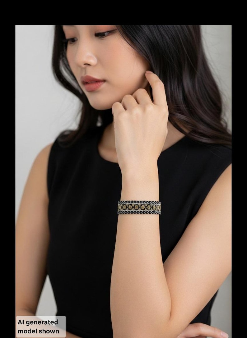 May include: A wide cuff bracelet featuring a repeating geometric pattern in black, gold, and silver tones. The design consists of a central row of gold-colored circular motifs bordered by thin silver lines and black edges with a textured appearance.