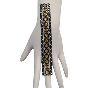 May include: A rectangular beaded bracelet featuring a geometric diamond pattern in black, gold, and silver seed beads. The design consists of a central column of gold diamonds bordered by black and silver vertical stripes, creating a structured look.
