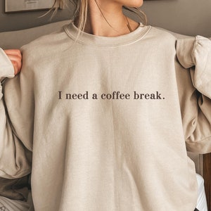May include: A beige sweatshirt with the text "I need a coffee break." printed in brown on the front.