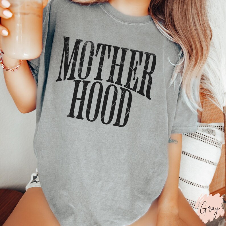 May include: A grey t-shirt with the text "MOTHERHOOD" printed in black with a distressed, vintage look.