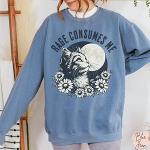 Embrace your feral energy with this distressed effect vintage-inspired Rage Consumes Me funny cat sweatshirt, printed on the ultra-comfy Comfort Colors 1566 sweatshirt. Designed for a relaxed, oversized fit, this unisex crewneck is perfect for cat lovers, introverts, and anyone who thrives on a little chaos. Featuring a moody cat, full moon, and floral details, this design brings together cottagecore and grunge aesthetics with a touch of humor.