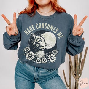 Embrace your feral energy with this distressed effect vintage-inspired Rage Consumes Me funny cat sweatshirt, printed on the ultra-comfy Comfort Colors 1566 sweatshirt. Designed for a relaxed, oversized fit, this unisex crewneck is perfect for cat lovers, introverts, and anyone who thrives on a little chaos. Featuring a moody cat, full moon, and floral details, this design brings together cottagecore and grunge aesthetics with a touch of humor.