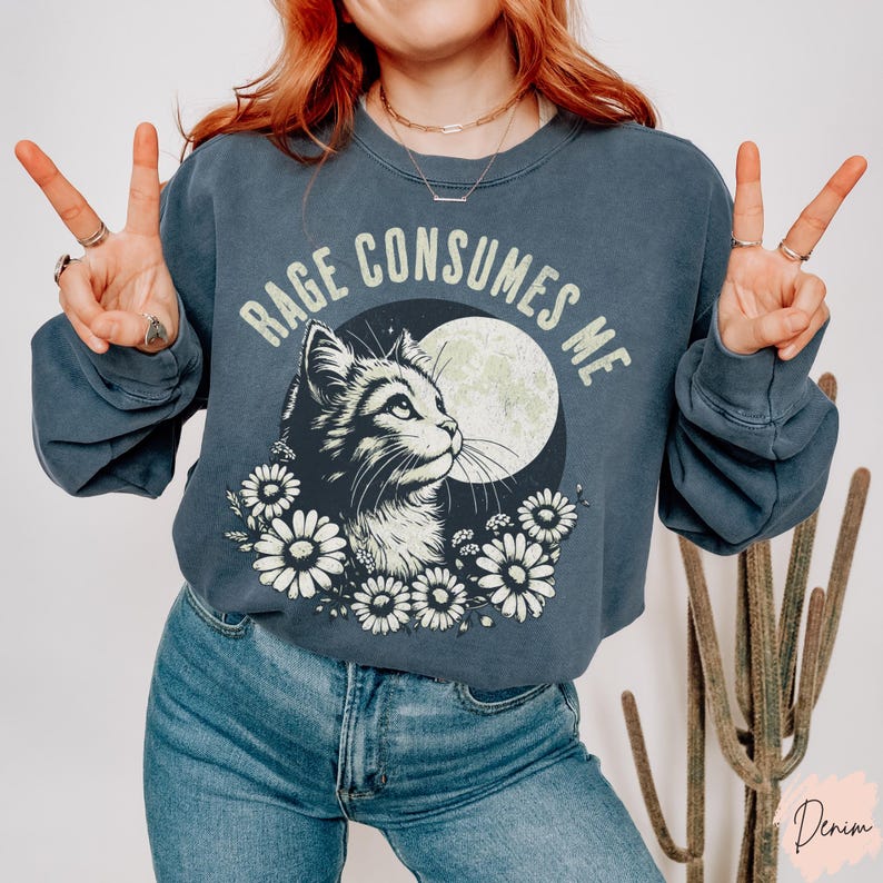 Embrace your feral energy with this distressed effect vintage-inspired Rage Consumes Me funny cat sweatshirt, printed on the ultra-comfy Comfort Colors 1566 sweatshirt. Designed for a relaxed, oversized fit, this unisex crewneck is perfect for cat lovers, introverts, and anyone who thrives on a little chaos. Featuring a moody cat, full moon, and floral details, this design brings together cottagecore and grunge aesthetics with a touch of humor.