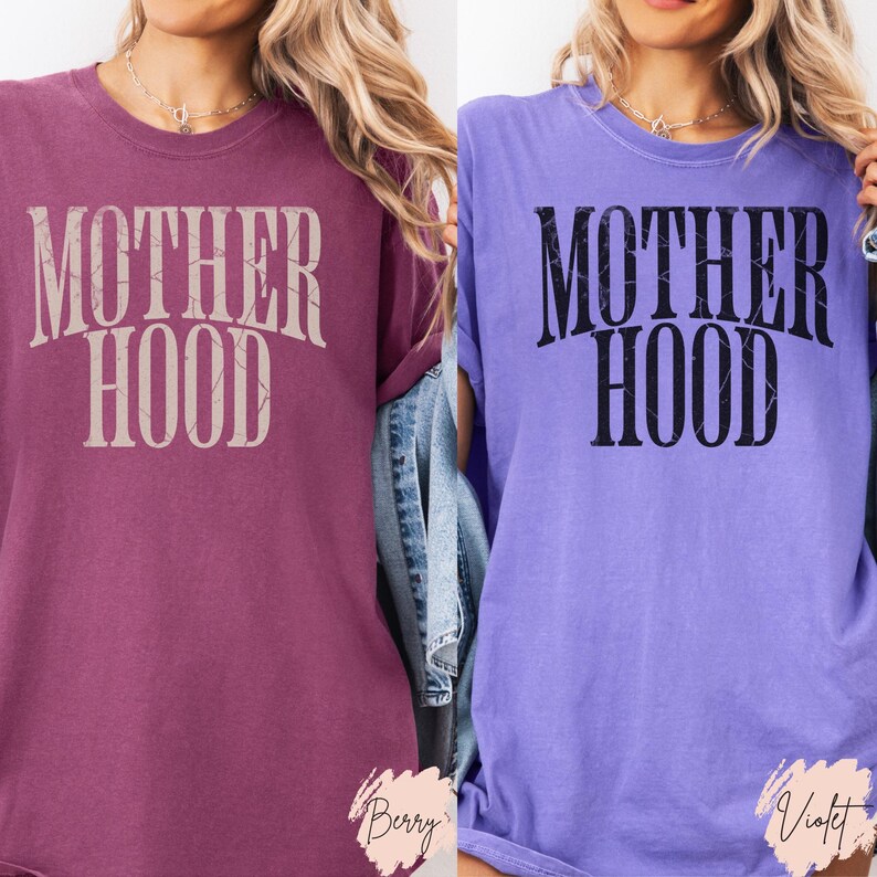 May include: Two t-shirts with the text "MOTHERHOOD" printed on them. One shirt is a deep purple colour and the other is a light purple colour.