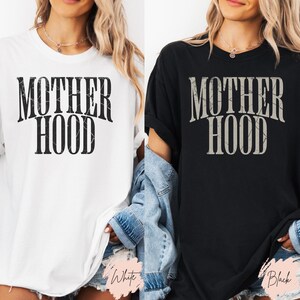 May include: Two t-shirts with the text "MOTHERHOOD" in a distressed font. One t-shirt is white and the other is black.