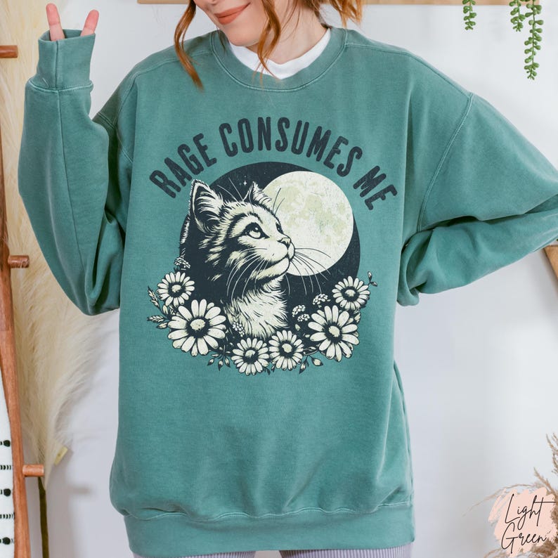 Embrace your feral energy with this distressed effect vintage-inspired Rage Consumes Me funny cat sweatshirt, printed on the ultra-comfy Comfort Colors 1566 sweatshirt. Designed for a relaxed, oversized fit, this unisex crewneck is perfect for cat lovers, introverts, and anyone who thrives on a little chaos. Featuring a moody cat, full moon, and floral details, this design brings together cottagecore and grunge aesthetics with a touch of humor.