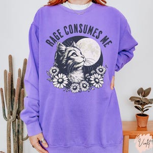 Embrace your feral energy with this distressed effect vintage-inspired Rage Consumes Me funny cat sweatshirt, printed on the ultra-comfy Comfort Colors 1566 sweatshirt. Designed for a relaxed, oversized fit, this unisex crewneck is perfect for cat lovers, introverts, and anyone who thrives on a little chaos. Featuring a moody cat, full moon, and floral details, this design brings together cottagecore and grunge aesthetics with a touch of humor.
