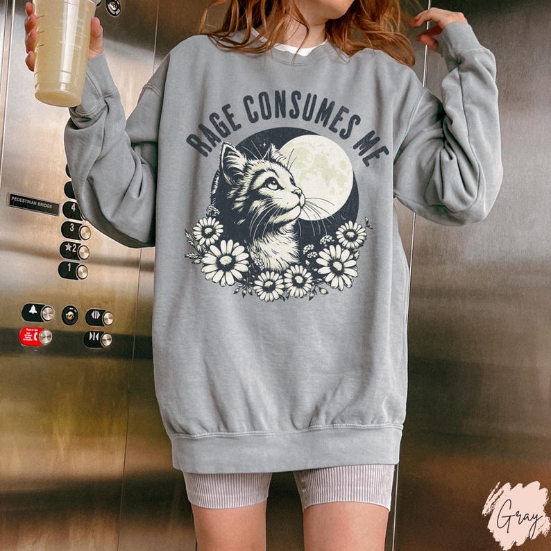 Embrace your feral energy with this distressed effect vintage-inspired Rage Consumes Me funny cat sweatshirt, printed on the ultra-comfy Comfort Colors 1566 sweatshirt. Designed for a relaxed, oversized fit, this unisex crewneck is perfect for cat lovers, introverts, and anyone who thrives on a little chaos. Featuring a moody cat, full moon, and floral details, this design brings together cottagecore and grunge aesthetics with a touch of humor.