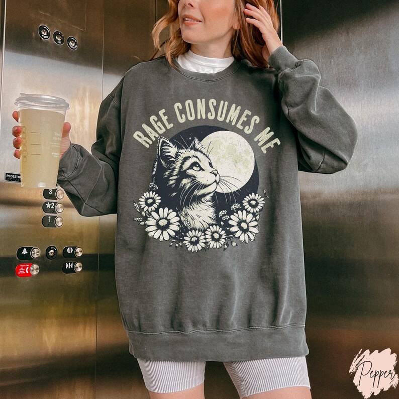 Embrace your feral energy with this distressed effect vintage-inspired Rage Consumes Me funny cat sweatshirt, printed on the ultra-comfy Comfort Colors 1566 sweatshirt. Designed for a relaxed, oversized fit, this unisex crewneck is perfect for cat lovers, introverts, and anyone who thrives on a little chaos. Featuring a moody cat, full moon, and floral details, this design brings together cottagecore and grunge aesthetics with a touch of humor.