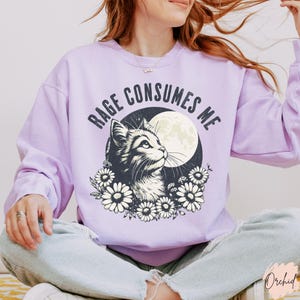 Embrace your feral energy with this distressed effect vintage-inspired Rage Consumes Me funny cat sweatshirt, printed on the ultra-comfy Comfort Colors 1566 sweatshirt. Designed for a relaxed, oversized fit, this unisex crewneck is perfect for cat lovers, introverts, and anyone who thrives on a little chaos. Featuring a moody cat, full moon, and floral details, this design brings together cottagecore and grunge aesthetics with a touch of humor.