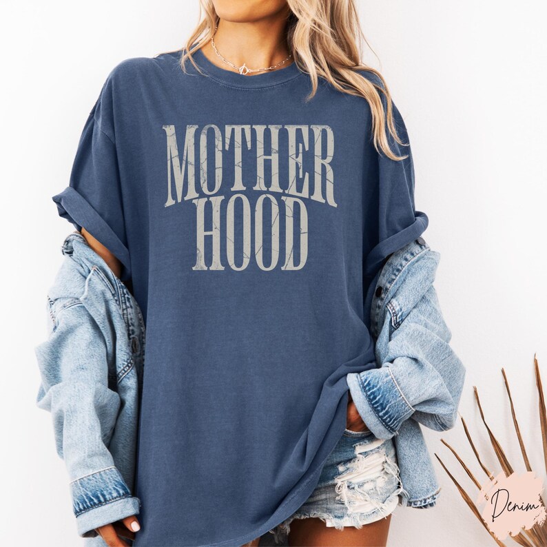 May include: A blue t-shirt with the text "MOTHERHOOD" printed in white on the front. The shirt is oversized and has a relaxed fit.