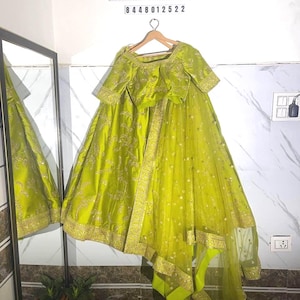 Könnte beinhalten: Ein limettengrünes formelles Kleid mit goldener Stickerei und einem passenden, durchsichtigen Dupatta. Das Kleid hängt an einem Holzkleiderbügel. Der Text "Ekdam Aesthetic" und eine Telefonnummer sind oben sichtbar.
