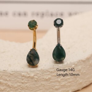 May include: Two belly button rings with teardrop-shaped green gemstones. One ring has a gold-colored curved bar, and the other has a silver-colored bar. The text "Gauge: 14G Length: 10mm" is visible.