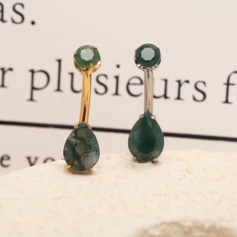 May include: Two drop earrings with green gemstones. One earring has a gold-colored post and setting, while the other has a silver-colored post and setting. The teardrop-shaped gemstones have a mottled appearance.