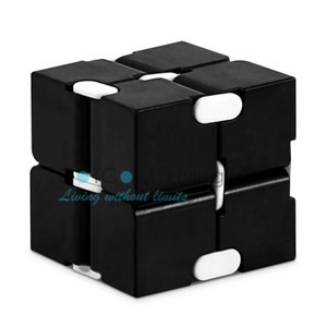 May include: Black and white infinity cube toy. The cube is made up of black rectangular blocks joined by white hinges. The text "Living without limits" is visible in the lower left corner.