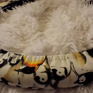 May include: A black and white steering wheel cover with a penguin design. The cover is made of fabric and has a yellow accent.