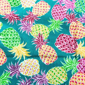 May include: A teal fabric with a repeating pattern of colorful pineapples. The pineapples are in shades of yellow, green, and pink, with red and purple tops. The design is tropical and vibrant.
