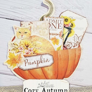 Puede incluir: Una calabaza de papel con un gato, flores y hojas. La calabaza est&aacute; decorada con una etiqueta que dice "Pumpkin". La artesan&iacute;a es parte de un conjunto m&aacute;s grande llamado "Cozy Autumn Ephemera Pocket" de Calico Collage.