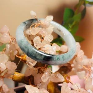 May include: A smooth, circular bangle bracelet featuring a marbled pattern of translucent white and deep forest green tones. The inner surface of the bangle displays a small white sticker with the printed text $90, indicating the item's price.