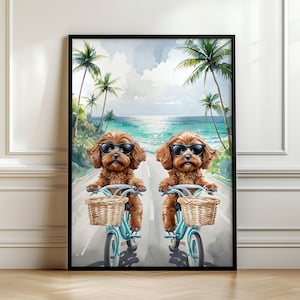 Op de afbeelding: Een ingelijste aquarelprint met twee bruine honden met zonnebrillen, die op blauwe fietsen met rieten manden rijden. De achtergrond toont een kustlandschap met palmbomen, een weg en de oceaan.