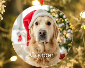 May include: A round, gold-colored Christmas ornament with a photo of a golden retriever wearing a Santa hat. The dog's name, "Cooper", is printed below the photo.