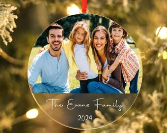 May include: A round, clear glass Christmas ornament with a photo of a family of four. The ornament has a gold rim and the text "The Evans Family 2024" printed on the bottom.