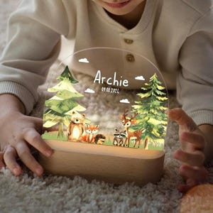 May include: A wooden night light with a clear acrylic insert featuring a woodland scene with a fox, deer, raccoon, and bear. The insert also has the name "Archie" and the date "09.08.2022" printed on it.