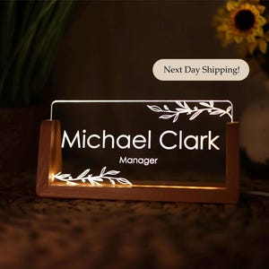 May include: A wooden desk nameplate with a clear acrylic insert. The insert has a white floral design and the text "Michael Clark Manager".