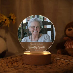 May include: A wooden base with a clear acrylic panel featuring a photo of a woman with the text "Forever in our hearts Dorothy Smith 1942-2024".