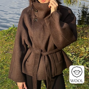 May include: A brown wool coat with a high collar and a belted waist. The coat has long sleeves and two buttons on the collar. The coat is made of wool and has a soft texture. The coat is a medium brown colour.